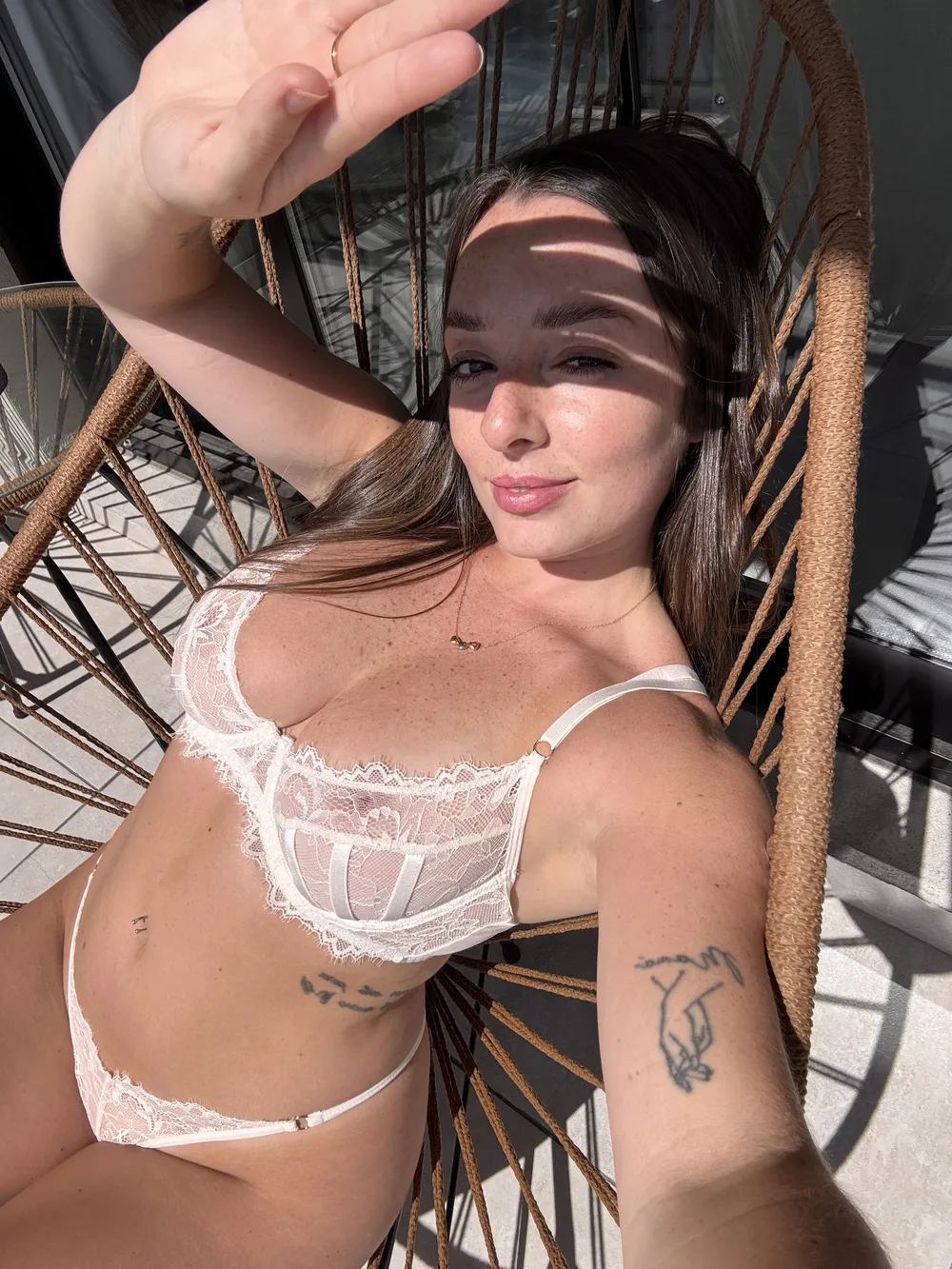 Sara (@saracore) relaxing in white lace lingerie while taking a sunlit selfie, showcasing her natural beauty and freckles.